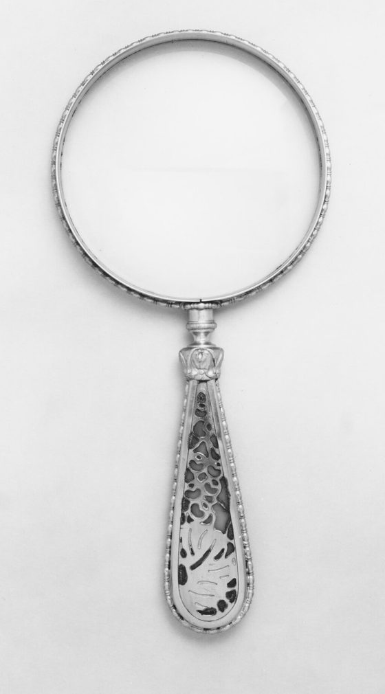 A silver hand magnifier with an open ring and a teardrop handle, photographed on a pale background